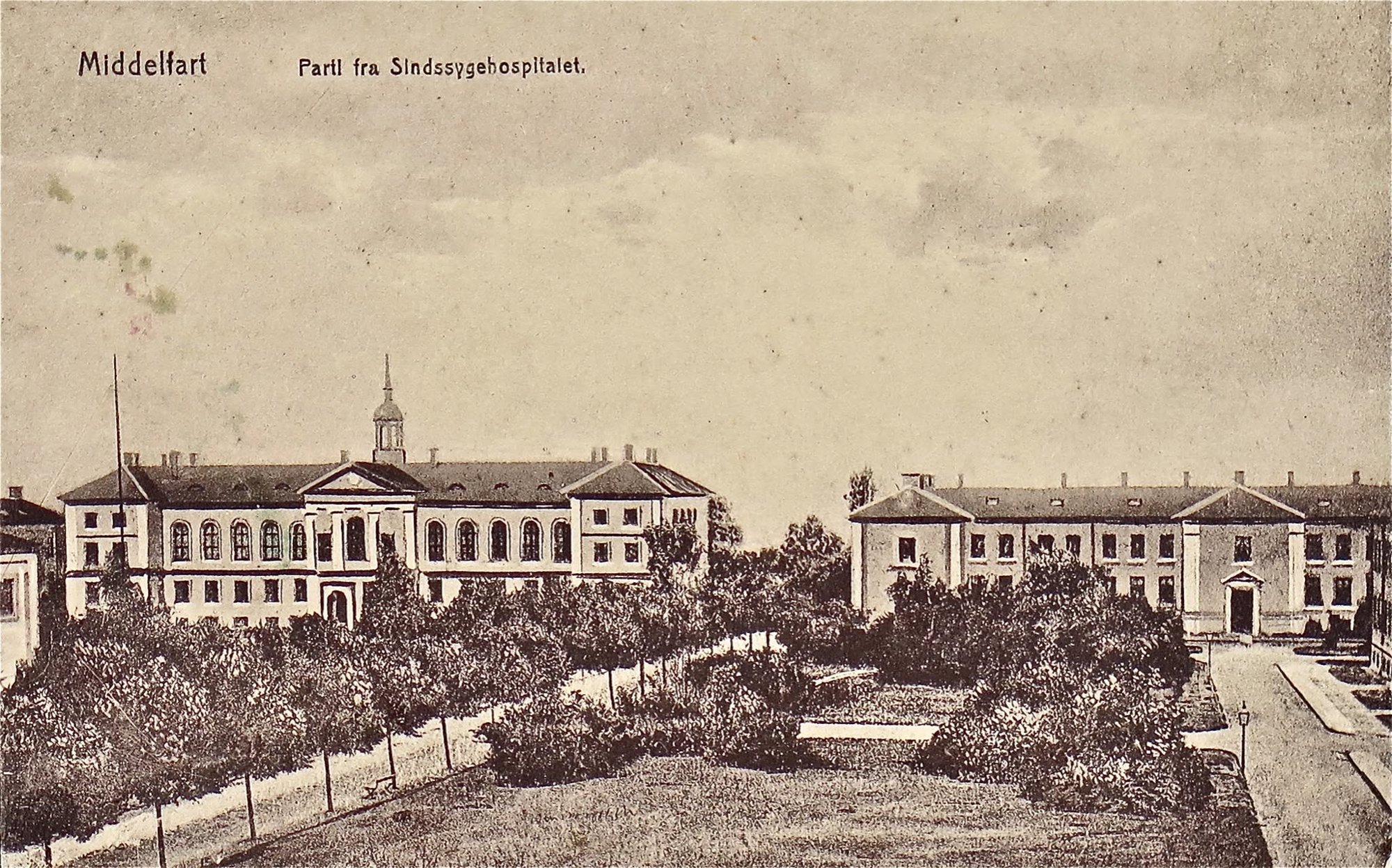 Den gamle sindssygeanstalt i Middelfart med dens gule murstensbygninger og kobberspir.