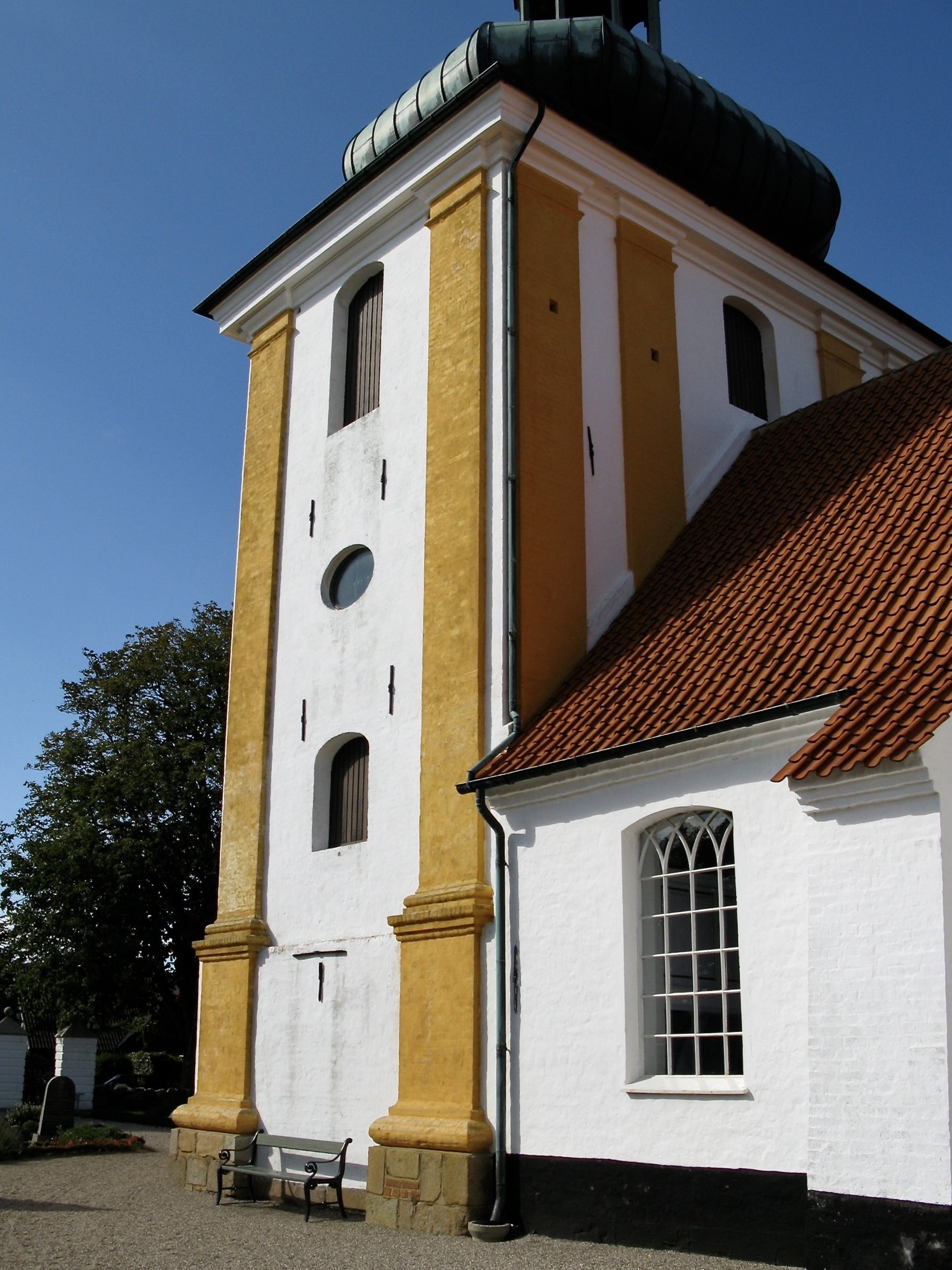 Husby Kirke med sit karakteristiske løgformede spir i det wedellsborgske landskab.